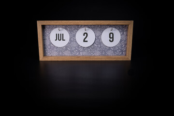 A wooden calendar block showing the date July 29th on a dark black background, save the date or date of event concept
