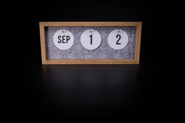 A wooden calendar block showing the date September 12th on a dark black background, save the date or date of event concept