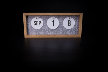 A wooden calendar block showing the date September 18th on a dark black background, save the date or date of event concept
