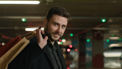 Naklejka premium Caucasian man shopper guy customer businessman stand in underground car parking carry shopping bags from shop mall supermarket buy presents gifts happy joyful tourist hold purchases sale black friday