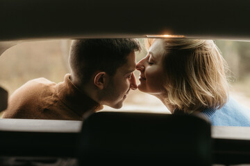 Intimate moment woman and man sitting in the open trunk of a car while traveling in autumn and kissing