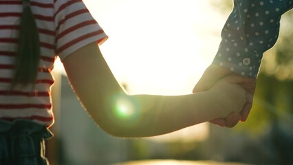 Happy family mother and daughter holding hands walking together at bright sun light summer park closeup. Little baby kid child and female parent arm enjoy outdoor weekend activity with love tenderness