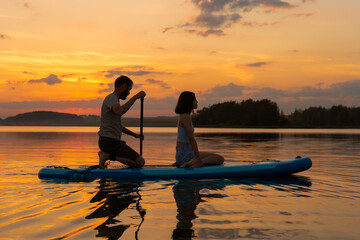 silhouette of couple paddleboarding at lake during sunset together. Concept of active family...