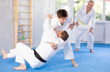 Men train to throw on the mat under the guidance of a judo coach