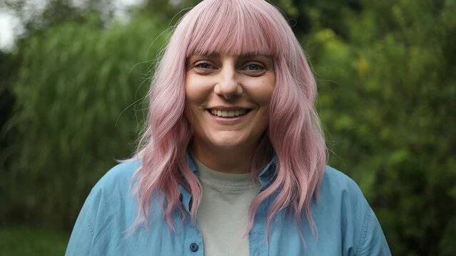 Close up photo of cute charming pink hair lady smile at camera outdoors at summer garden. High quality FullHD footage
