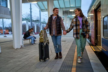 Hand in hand, a couple strolls along the train platform, their journey together just beginning,...