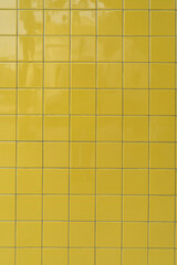 Section of wall covered with neatly arranged yellow tiles. Square-shaped material have uniform in size and color creating consistent and orderly look. Glossy surface