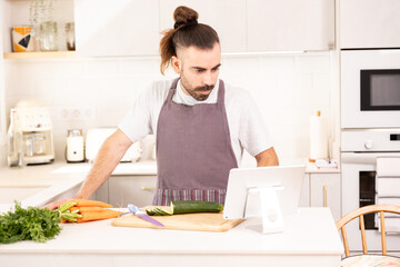 Fototapeta na wymiar long-haired man cooking at home looking at tablet, chopping vegetables