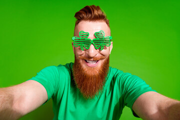 Portrait of toothy beaming guy with red beard wear green t-shirt in shamrock glasses making selfie...