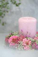 Różowa świeca otoczona wiankiem z letnich, różowych kwiatów. Cynie.