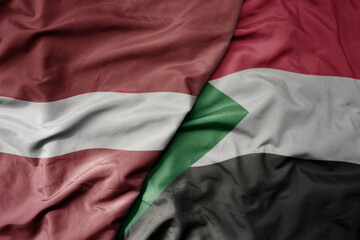 big waving national colorful flag of sudan and national flag of latvia.