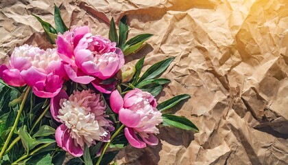 tender bouquet of pink peonies flowers in sunlight on wrinkled craft paper background