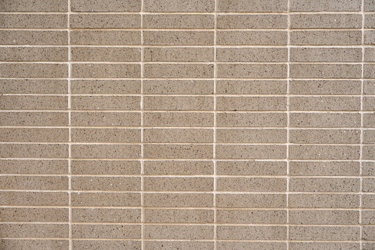 Wall covered with beige symmetrical and minimalistic tiles. Square and smooth material separated by light-colored grout lines. Concept of texture and pattern