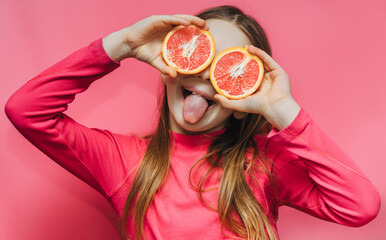 Little cute funny girl using grapefruit instead of eyes, having fun and fooling around in the...