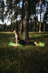 Yoga cobra pose by woman in black suit on green grass in the park around pine trees. Alone yoga in the garden in the morning, stretch back. Healthy lifestyle. 