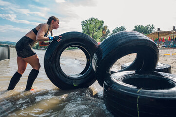 Muscular woman pushing tractor tire out of the water during an OCR race