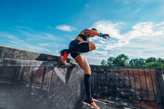 Woman participating in an obstacle course race and jumping over the fence