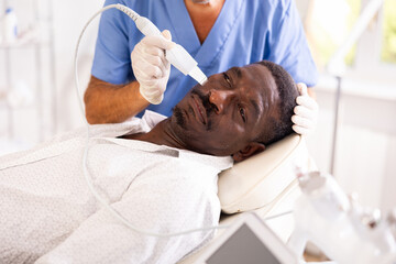 African man in cosmetologists office receives cleansing and rejuvenating facial skin care...