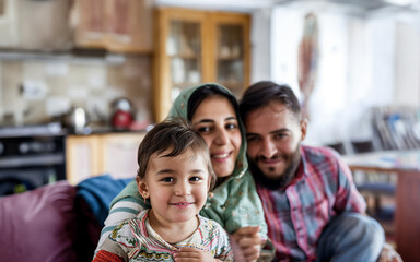 Candid moment of a Syrian immigrant family at home, with father, mother, and children sharing laughter in a warm, familial setting.

