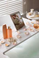 Obraz na płótnie Canvas Wooden tray with tablet, wine, toiletries and flower petals on bathtub in bathroom