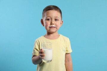 Cute boy with milk mustache holding glass of tasty dairy drink on light blue background