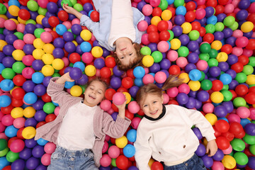Happy little kids lying on many colorful balls, top view