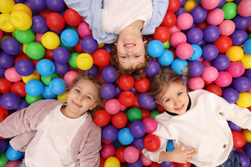 Fototapeta na wymiar Happy little kids lying on many colorful balls, top view