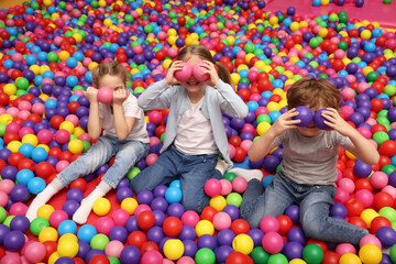 Happy little kids sitting on colorful balls in ball pit
