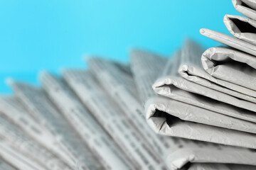 Stack of newspapers on light blue background, closeup. Journalist's work