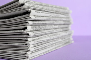 Stack of newspapers on light violet background, closeup. Journalist's work