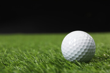 Golf ball on green grass against black background, space for text