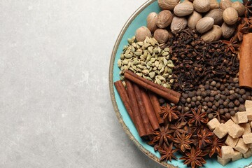 Different spices and nuts in bowl on light gray textured table, top view. Space for text