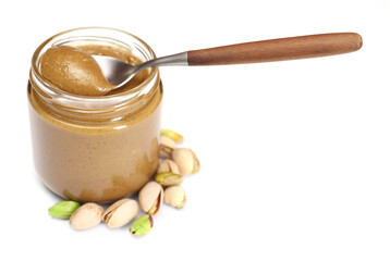Tasty nut paste in jar, spoon and pistachios isolated on white