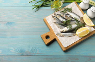 Fresh raw sprats, dill, oil and cut lemon on light blue wooden table, flat lay. Space for text