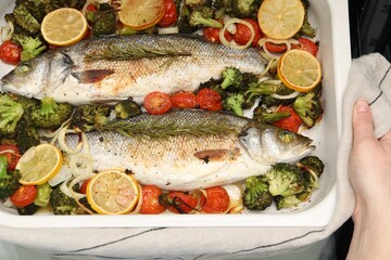 Woman holding baking dish with delicious fish and vegetables, top view