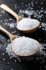 Organic salt in spoons on black wooden table, closeup