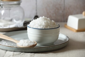 Organic salt in bowl and wooden spoon on table, closeup