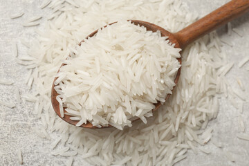 Raw basmati rice and wooden spoon on grey table, top view