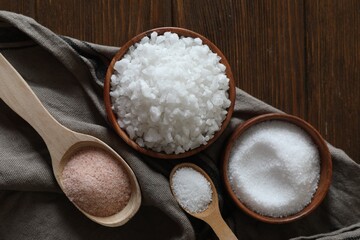 Different types of organic salt on wooden table, flat lay