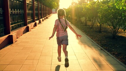 Child runs along sidewalk on street in sun. Children dream, happiness concept. Joyful little girl...