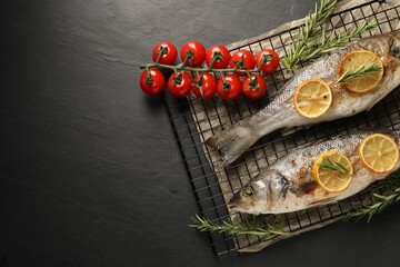 Obraz na płótnie Canvas Baked fish with tomatoes, rosemary and lemon on black textured table, top view. Space for text