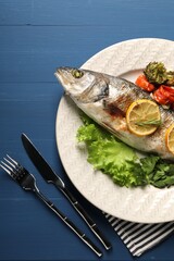 Delicious baked fish and vegetables served on blue wooden table, top view