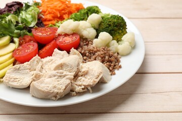 Balanced diet and healthy foods. Plate with different delicious products on light wooden table, closeup