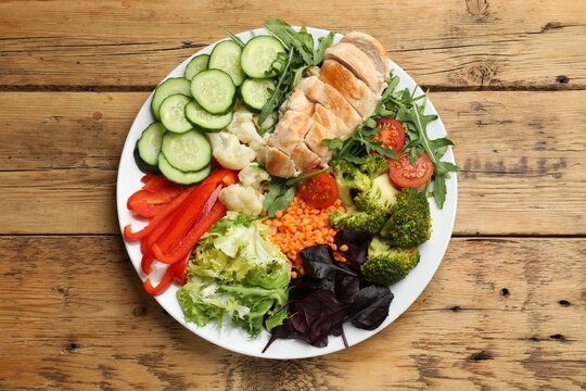 Balanced diet and healthy foods. Plate with different delicious products on wooden table, top view