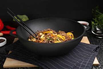 Stir-fry. Tasty noodles with vegetables, meat and chopsticks in wok on dark textured table