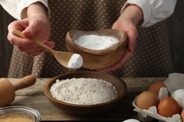 Making dough. Woman adding baking powder to flour at wooden table, closeup