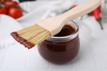 Marinade in jar and basting brush on white table, closeup