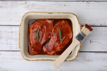 Raw marinated meat, rosemary and basting brush on white wooden table, top view