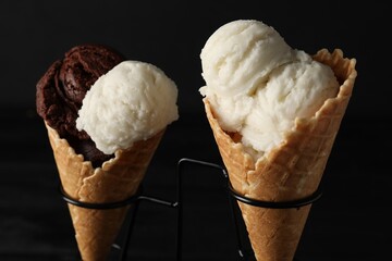 Ice cream scoops in wafer cones on stand against dark background, closeup