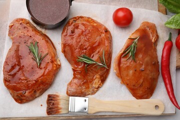 Raw marinated meat, rosemary, products and basting brush on table, flat lay